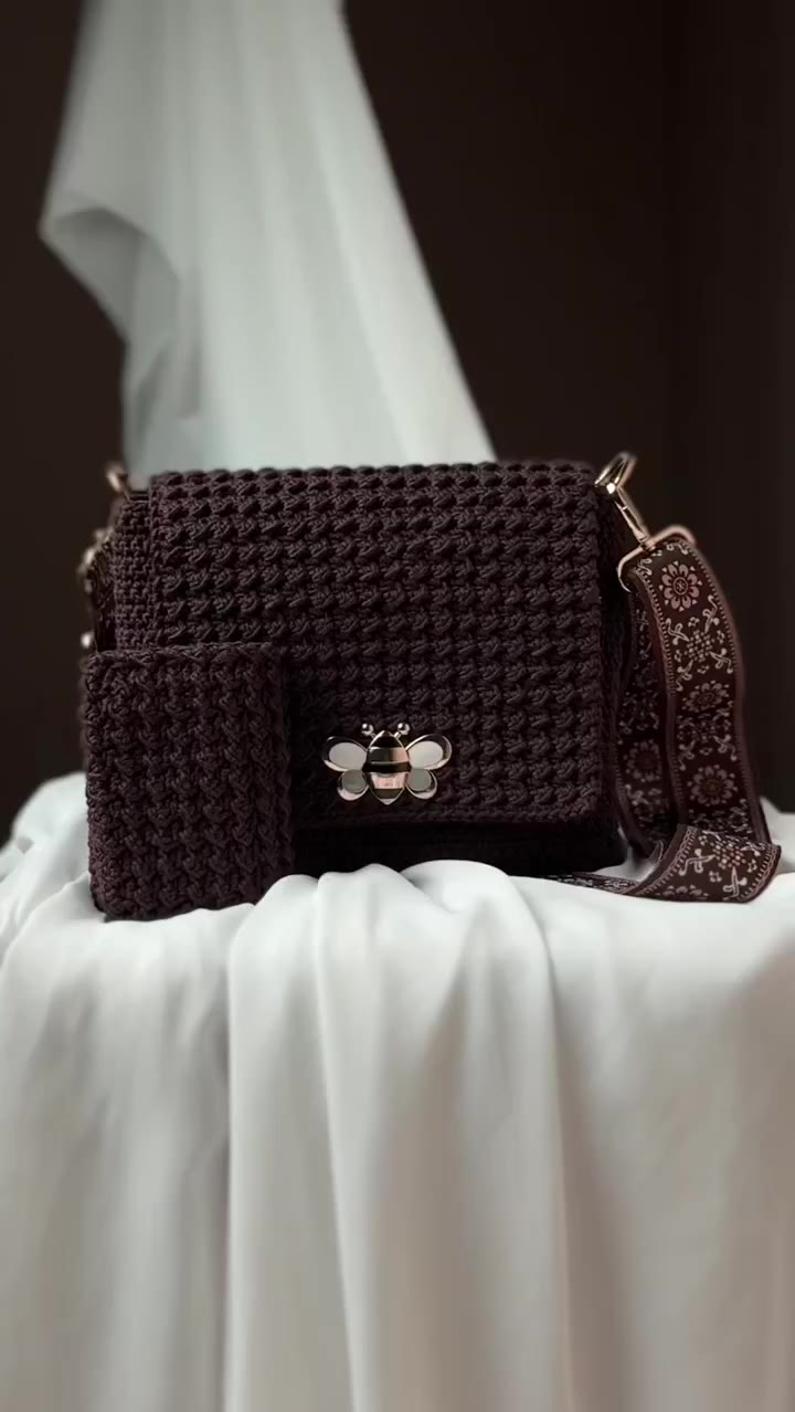 A brown crochet Luvra bag with a bee clasp, set on white fabric